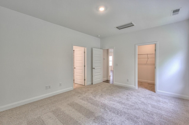 unfurnished bedroom with light carpet, visible vents, a spacious closet, and baseboards