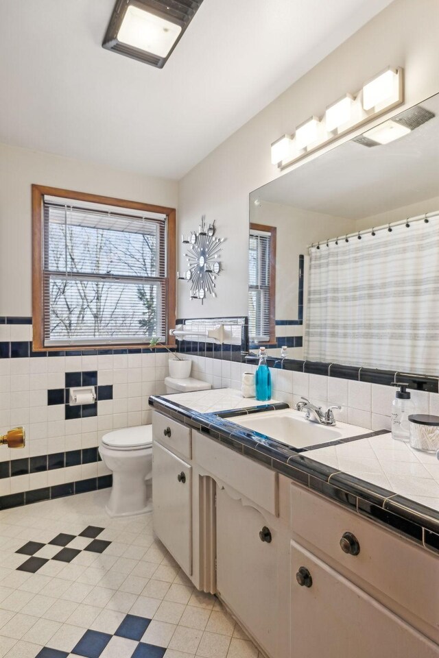 full bathroom featuring toilet, wainscoting, tile walls, and vanity