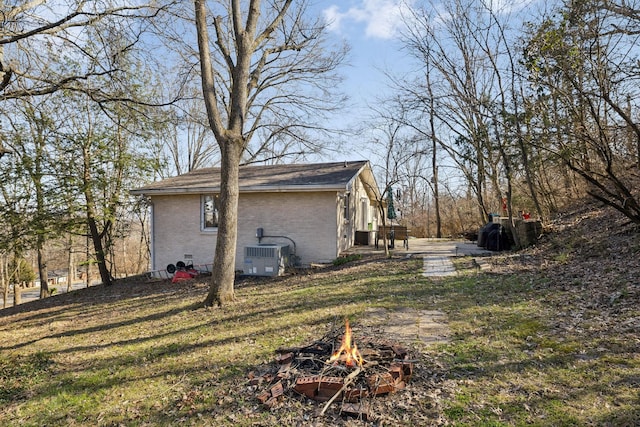 view of home's exterior with crawl space, brick siding, an outdoor fire pit, and a lawn