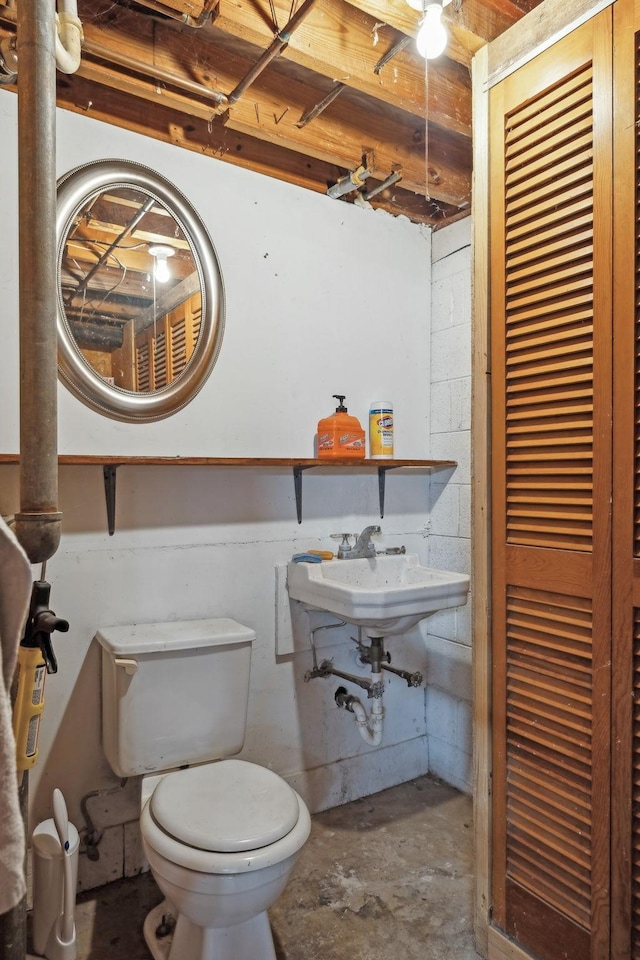 half bathroom featuring concrete floors, a sink, toilet, and concrete block wall