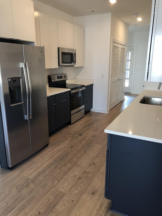 kitchen featuring stainless steel appliances, light countertops, a sink, and wood finished floors