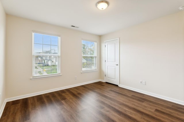 empty room with dark wood-style floors, baseboards, and visible vents