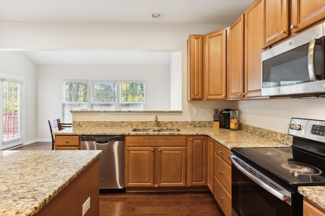 kitchen featuring light stone counters, dark wood-style flooring, a peninsula, stainless steel appliances, and a sink