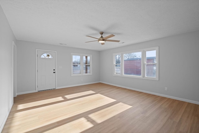 interior space featuring a textured ceiling, a ceiling fan, light wood-style flooring, and baseboards