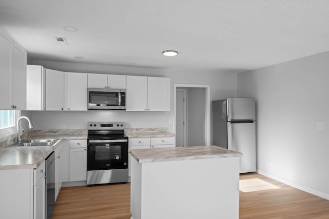 kitchen featuring light wood finished floors, light countertops, appliances with stainless steel finishes, white cabinetry, and a sink