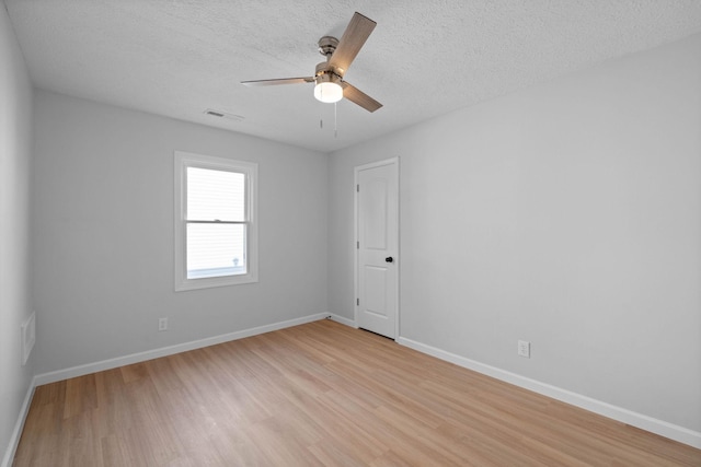 empty room featuring visible vents, light wood-style flooring, ceiling fan, a textured ceiling, and baseboards