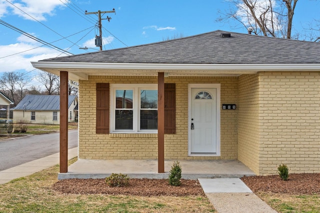 view of exterior entry with a shingled roof and brick siding