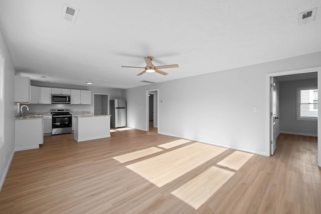 unfurnished living room with light wood-type flooring, a sink, visible vents, and baseboards