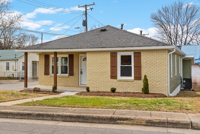 bungalow-style house featuring central AC unit, a shingled roof, and brick siding