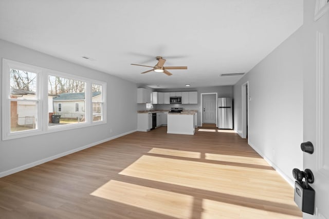 unfurnished living room with a sink, a ceiling fan, visible vents, baseboards, and light wood finished floors