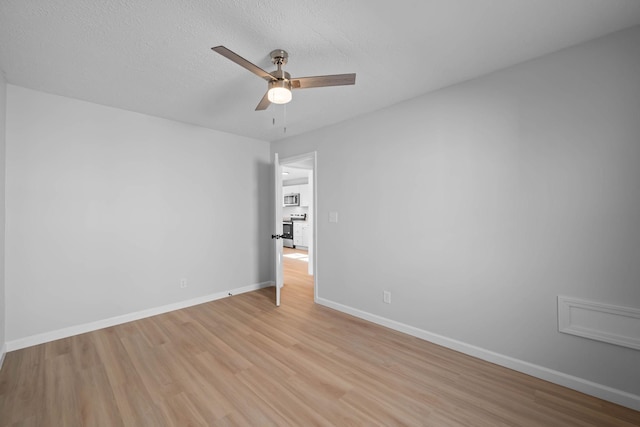 spare room featuring light wood-type flooring, ceiling fan, a textured ceiling, and baseboards