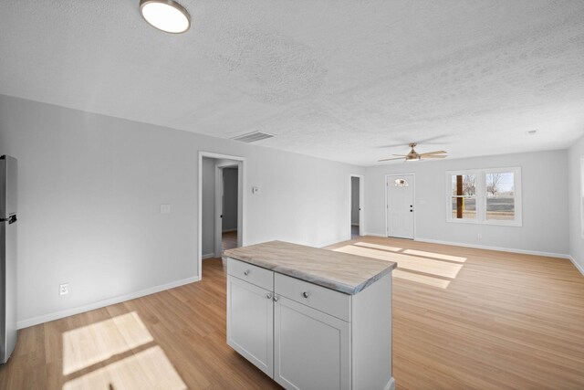 unfurnished living room featuring light wood-style flooring, a textured ceiling, visible vents, and baseboards