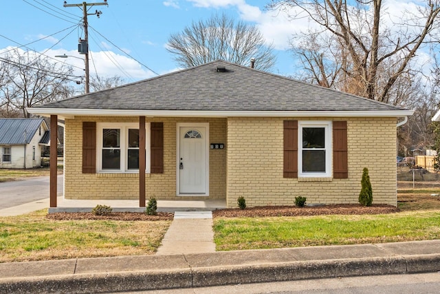 bungalow featuring covered porch, brick siding, and a shingled roof