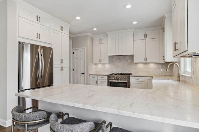 kitchen with decorative backsplash, appliances with stainless steel finishes, light stone counters, a peninsula, and premium range hood