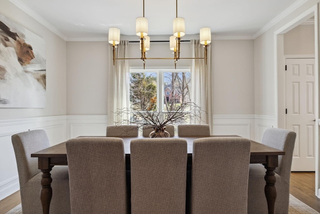 dining space with ornamental molding, wainscoting, wood finished floors, and an inviting chandelier