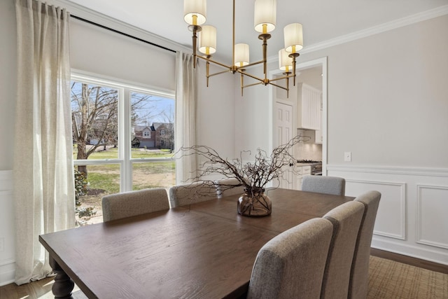 dining room featuring a wainscoted wall, ornamental molding, wood finished floors, a chandelier, and a decorative wall