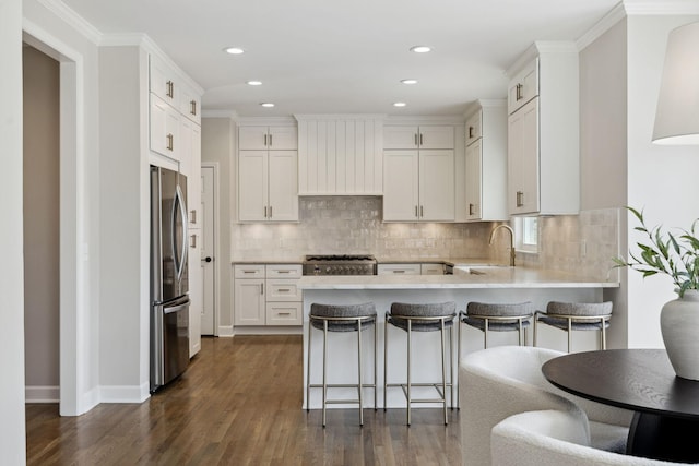 kitchen with stove, dark wood-type flooring, freestanding refrigerator, a sink, and a peninsula