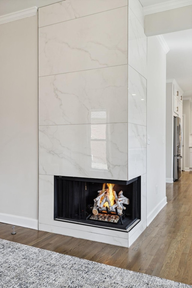 details featuring a fireplace, ornamental molding, freestanding refrigerator, wood finished floors, and baseboards