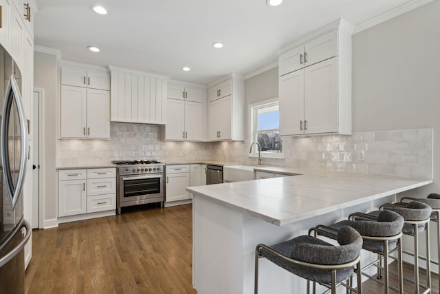 kitchen featuring stainless steel appliances, a peninsula, a sink, and white cabinetry