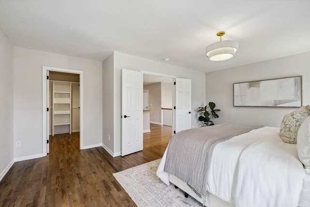 bedroom with a closet, a spacious closet, baseboards, and wood finished floors