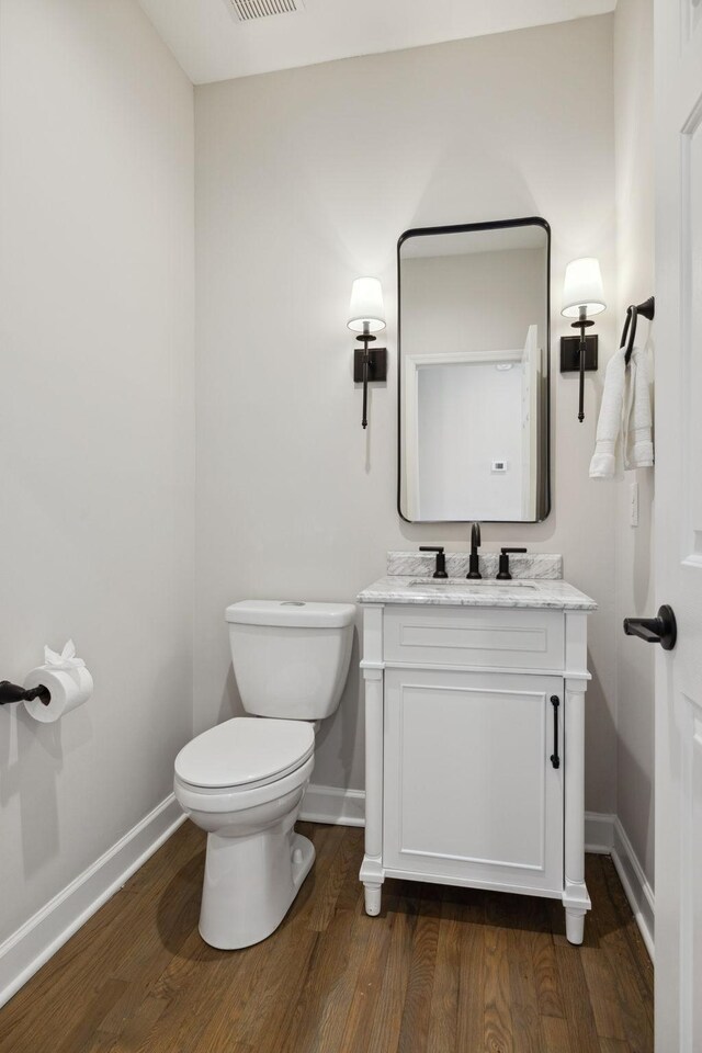 half bath featuring toilet, wood finished floors, visible vents, vanity, and baseboards