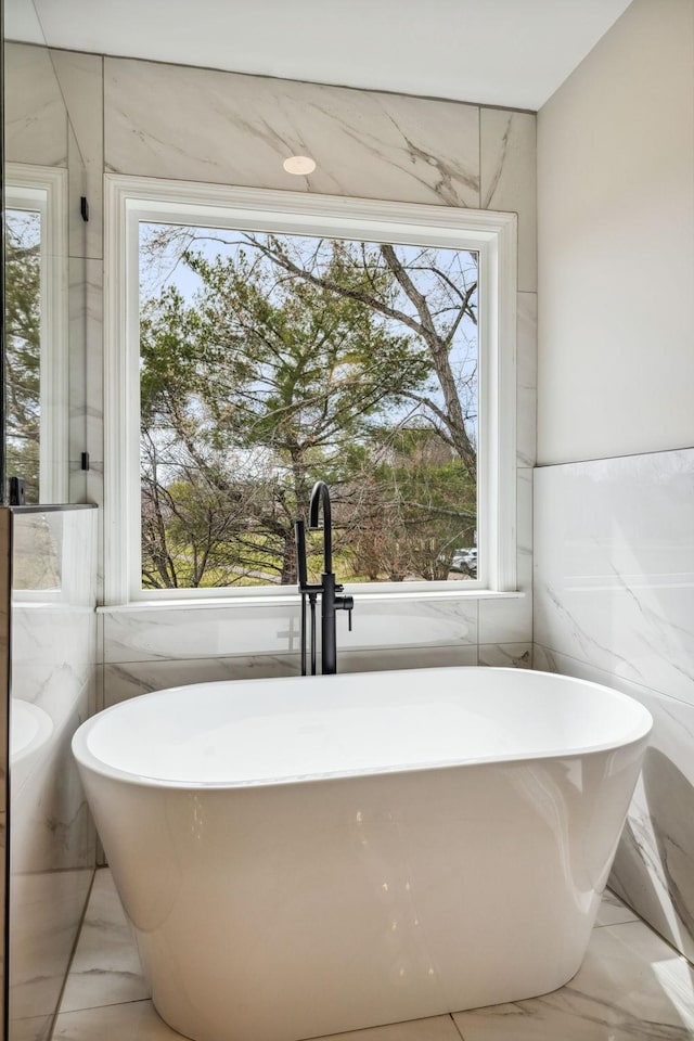 bathroom featuring a sink, marble finish floor, a freestanding bath, and a wealth of natural light