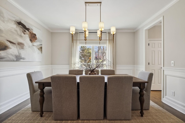 dining space with a wainscoted wall, ornamental molding, wood finished floors, and a notable chandelier