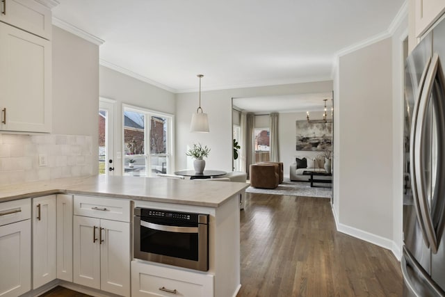 kitchen featuring a peninsula, ornamental molding, appliances with stainless steel finishes, tasteful backsplash, and dark wood finished floors