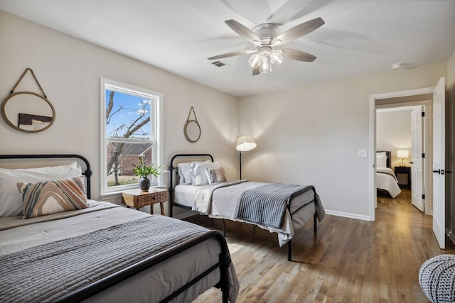 bedroom featuring ceiling fan, wood finished floors, visible vents, and baseboards