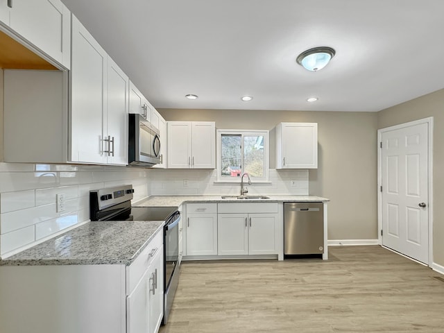 kitchen featuring stainless steel appliances, light stone counters, light wood-type flooring, and a sink