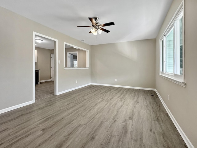 empty room with wood finished floors, a ceiling fan, and baseboards