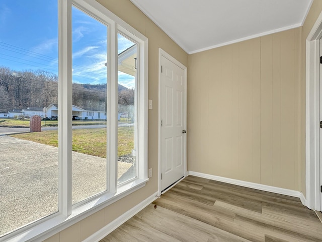 doorway to outside with baseboards, plenty of natural light, wood finished floors, and crown molding