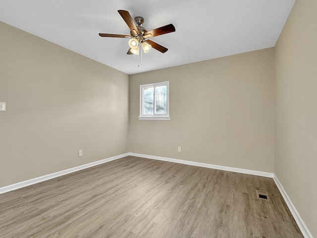 empty room with a ceiling fan, visible vents, baseboards, and wood finished floors