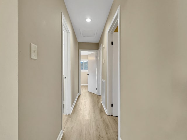 hallway featuring light wood finished floors, attic access, visible vents, and baseboards