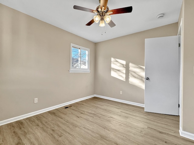 spare room with ceiling fan, visible vents, baseboards, and wood finished floors