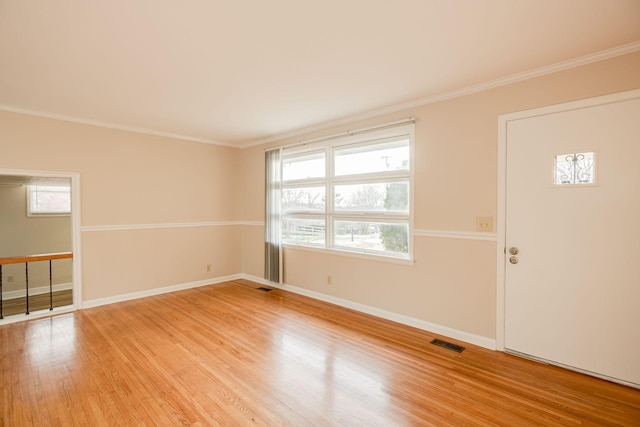 spare room featuring ornamental molding, light wood-type flooring, visible vents, and baseboards