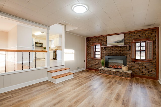 unfurnished living room with baseboards, brick wall, light wood-style flooring, ornamental molding, and a brick fireplace