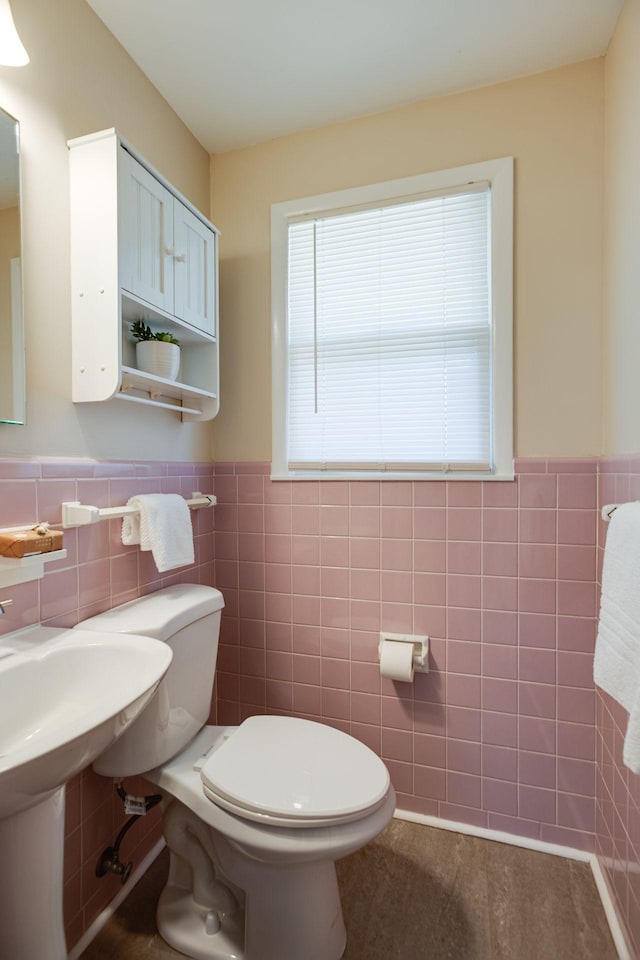 bathroom with toilet, a wainscoted wall, and tile walls