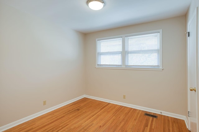 spare room with light wood-type flooring, visible vents, and baseboards