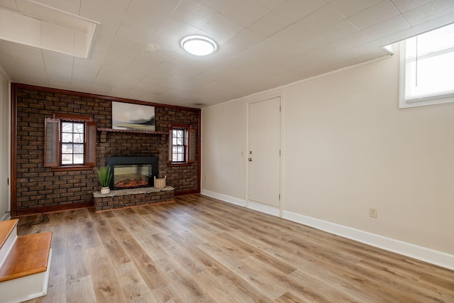 unfurnished living room with a wealth of natural light, a brick fireplace, brick wall, and wood finished floors