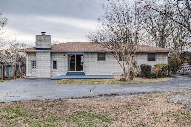 rear view of house featuring a chimney, fence, aphalt driveway, and brick siding