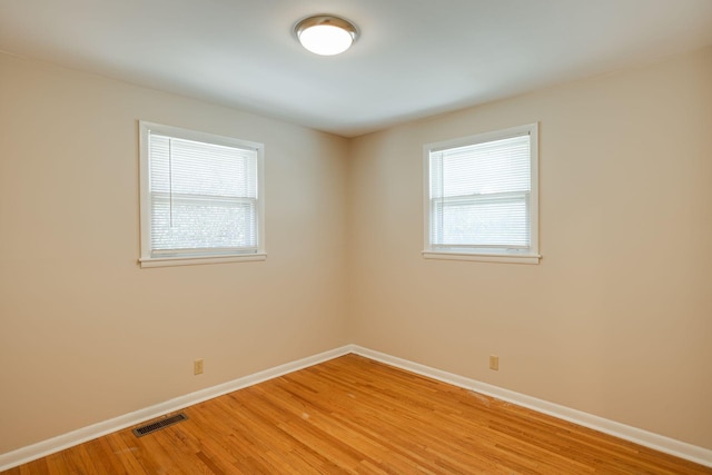 unfurnished room with a wealth of natural light, light wood-type flooring, visible vents, and baseboards