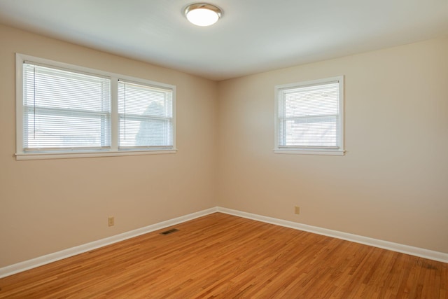 empty room with light wood-style flooring, visible vents, and baseboards