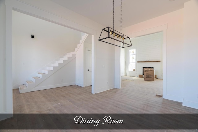 unfurnished dining area featuring stairs, a fireplace, wood finished floors, and baseboards