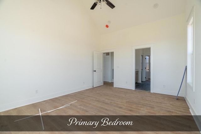 unfurnished bedroom featuring ensuite bath, baseboards, high vaulted ceiling, and wood finished floors