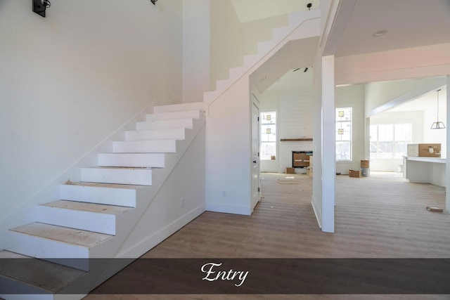 stairway with a fireplace, wood finished floors, a towering ceiling, and baseboards