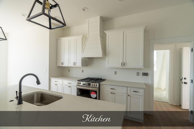 kitchen with white cabinets, custom range hood, stainless steel range with gas stovetop, wood finished floors, and a sink