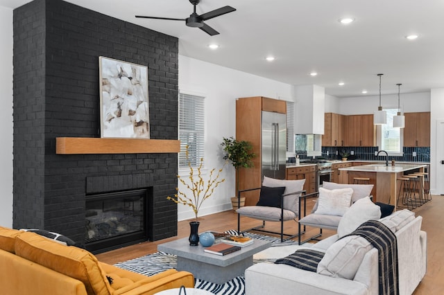 living area featuring ceiling fan, recessed lighting, baseboards, light wood-style floors, and a brick fireplace