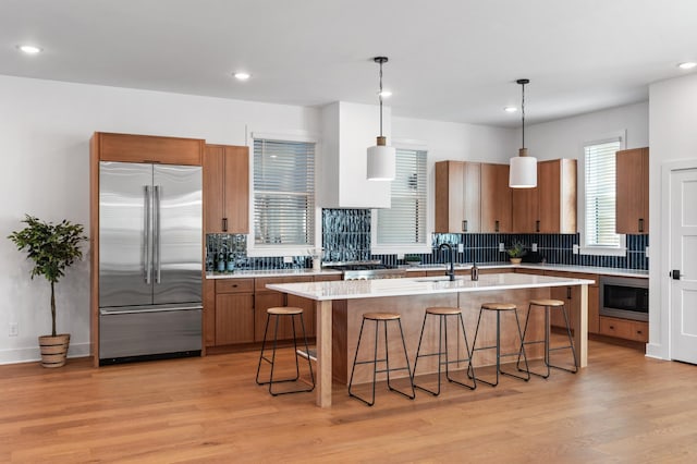 kitchen with light countertops, light wood finished floors, a kitchen breakfast bar, and built in appliances