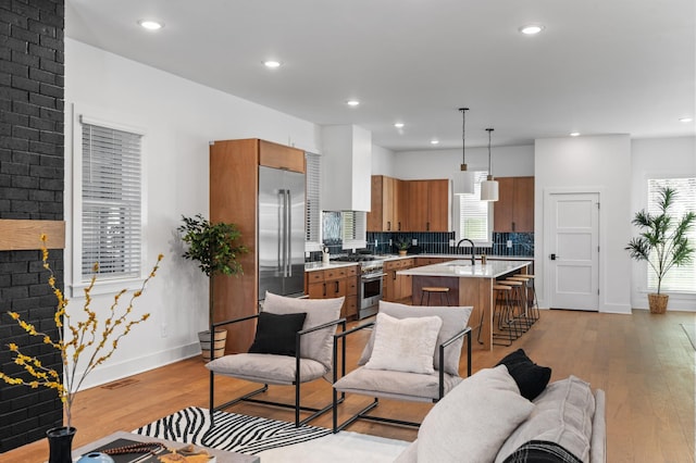 kitchen with a fireplace, light wood finished floors, high end appliances, light countertops, and brown cabinetry